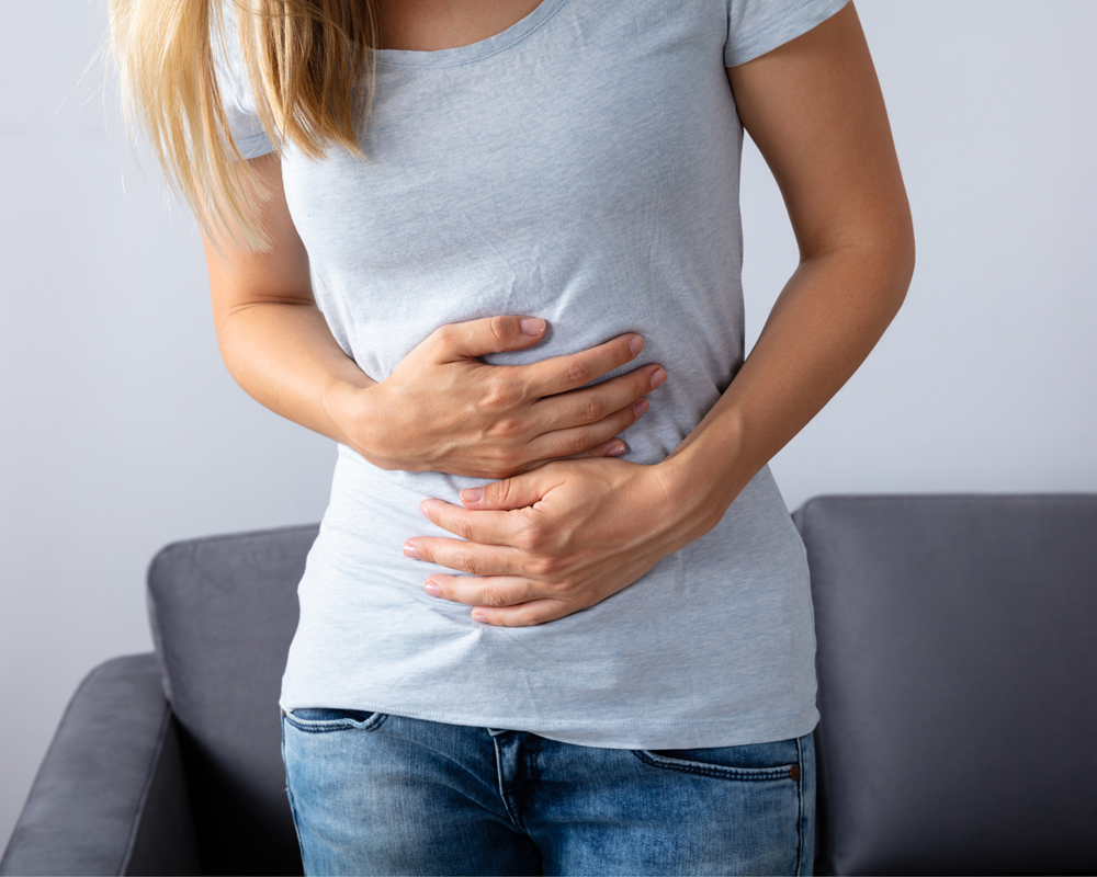 Frau hält sich den Bauch, weil sie unter stressbedingten Magenbeschwerden leidet.
