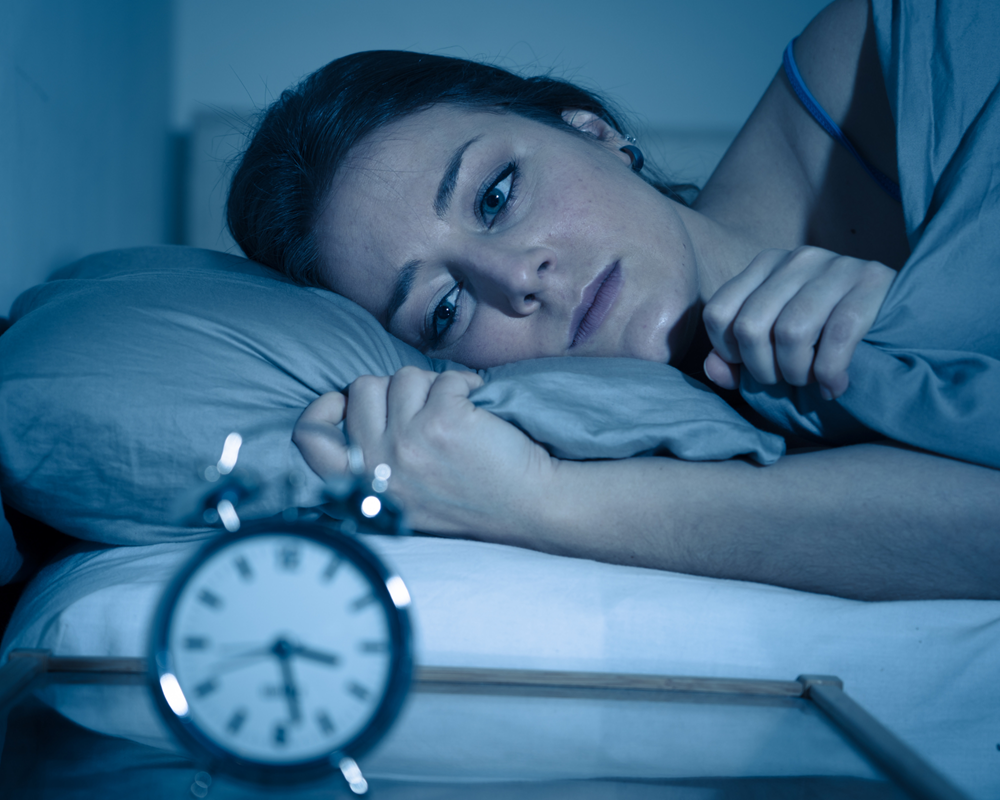 Frau schaut nachts auf die Uhr, nachdem sie erneut mitten in der Nacht aufgewacht ist.